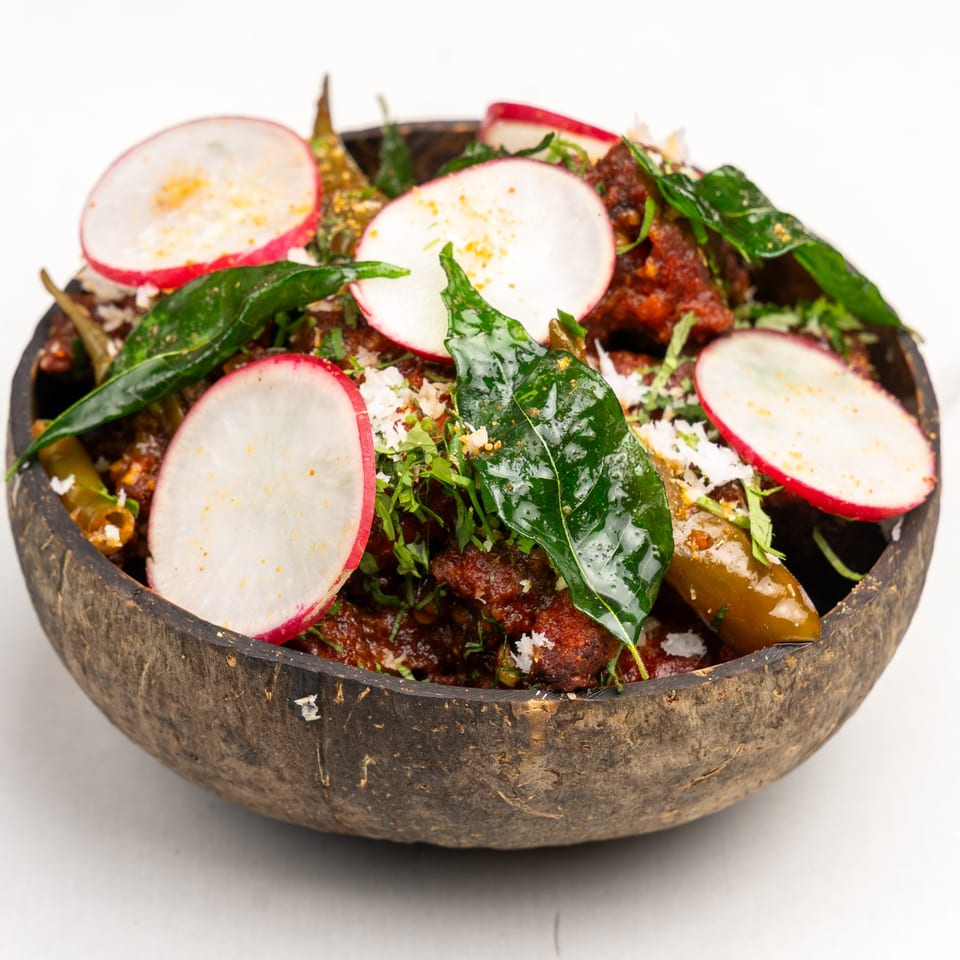 Gazab's Indian dish with red sauce, green leaves, radishes, and peppers in a coconut shell bowl.