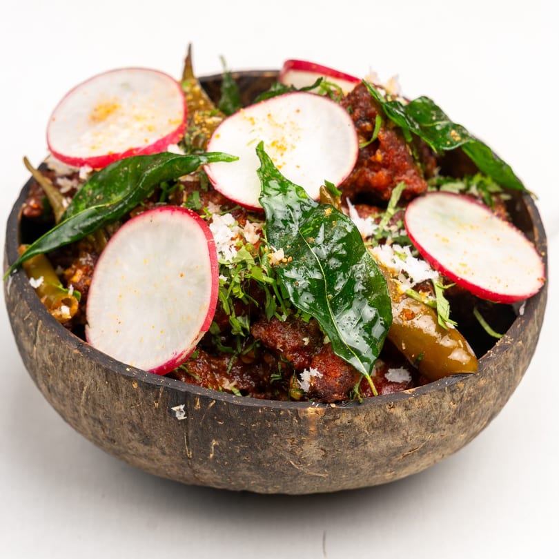 Gazab's Indian dish with red sauce, green leaves, radishes, and peppers in a coconut shell bowl.