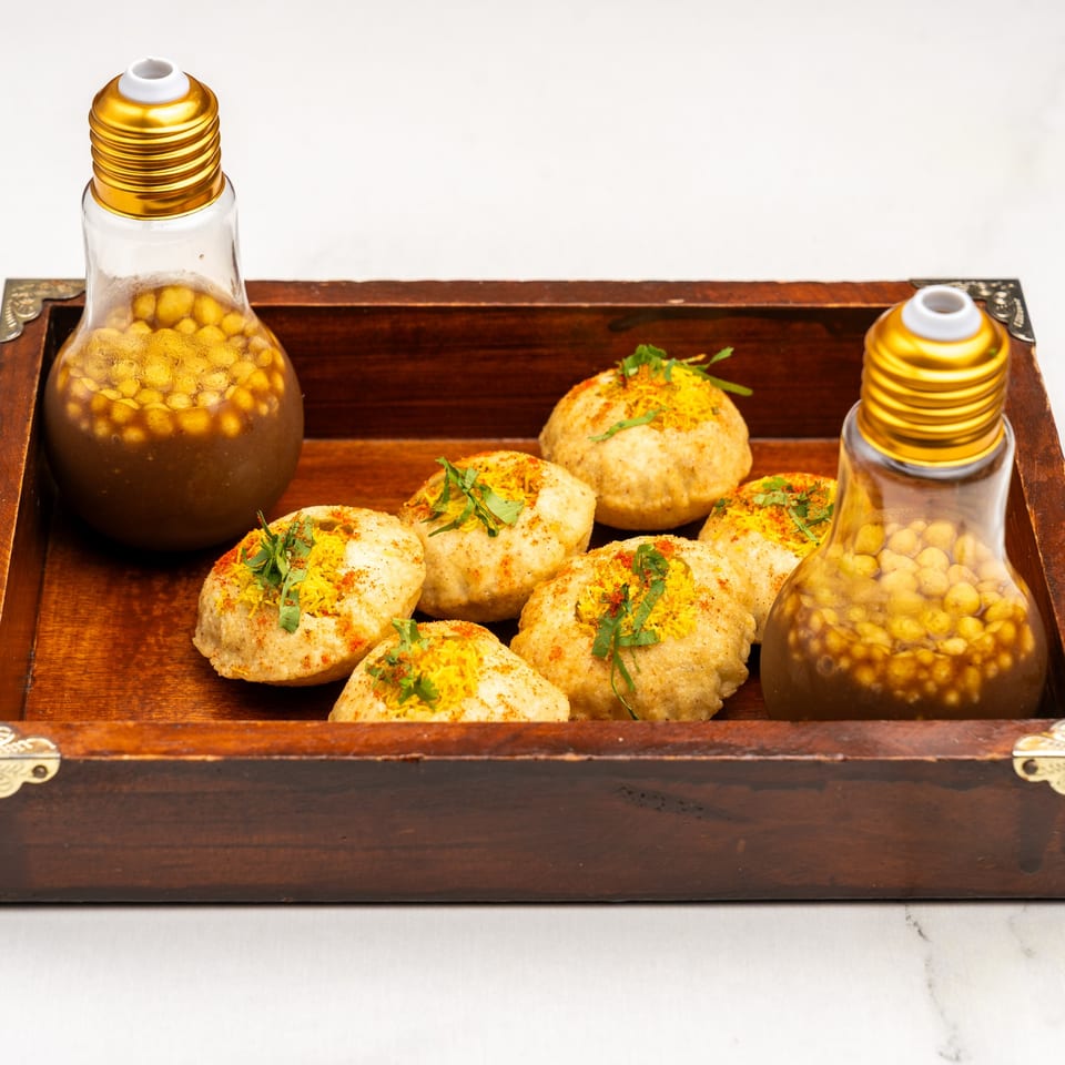 Gazab's pani puri, with six puris topped with spices and herbs, and two lightbulb-shaped bottles of pani.