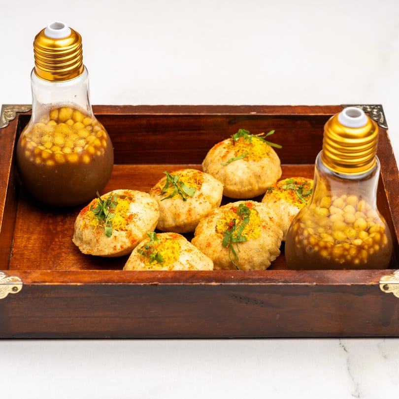 Gazab's pani puri, with six puris topped with spices and herbs, and two lightbulb-shaped bottles of pani.