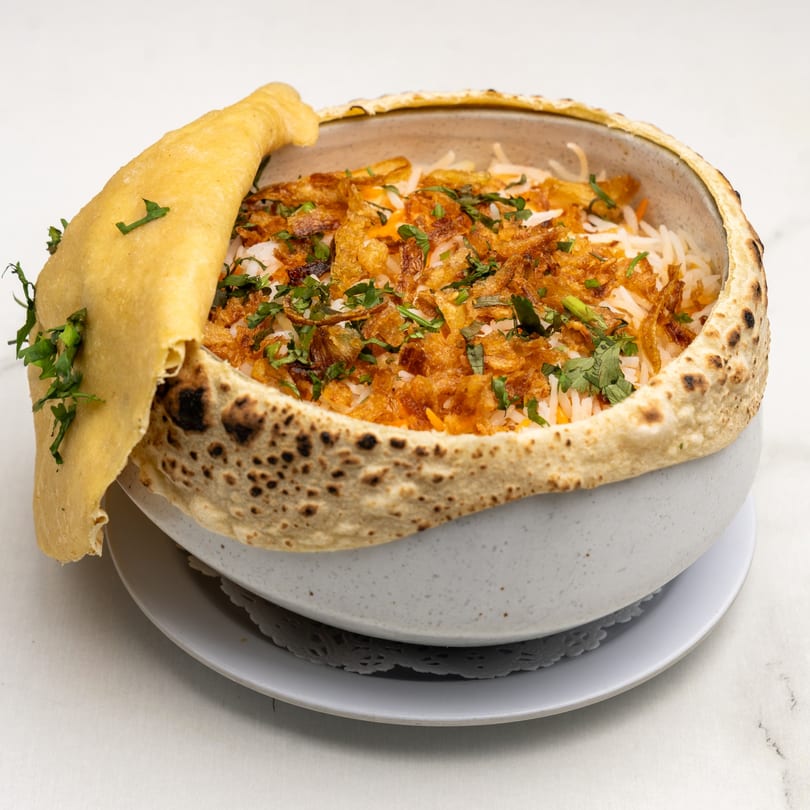 Gazab's Indian biryani in a clay pot, topped with crispy fried onions and fresh cilantro.