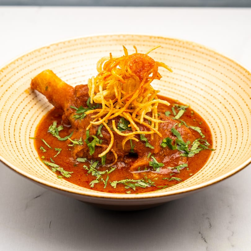 Gazab's Indian lamb shank in a rich red sauce, garnished with cilantro and crispy fried onions.