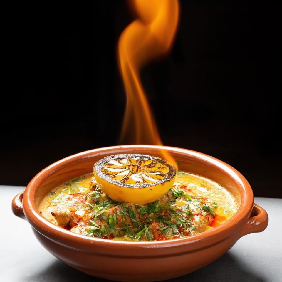 Flaming dish in a terracotta bowl with a charred lemon half and fresh herbs.