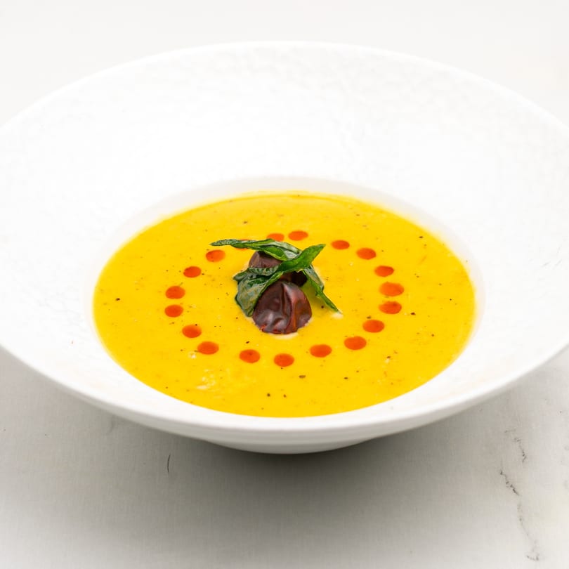 Bright yellow Indian soup with red oil dots and green herb garnish in a white bowl.