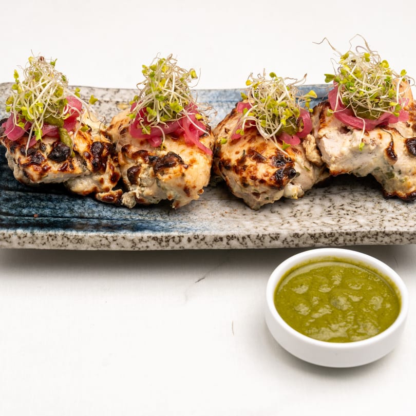 Four pieces of grilled Indian chicken tikka, garnished with sprouts and pickled onions, with green chutney.
